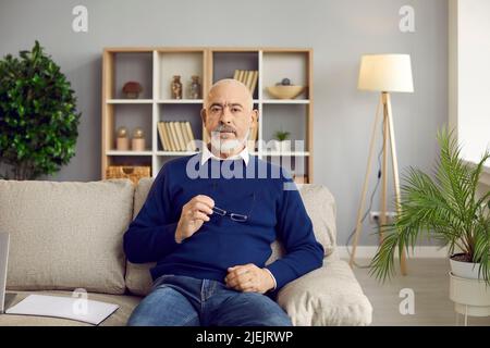 Portrait of handsome and stylish unshaven bald senior man sitting on sofa in home office. Stock Photo