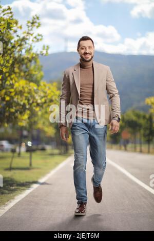 Full length portrait of a young man in a beige suit and jeans walking towards camera on an asphalt pedestrian lane Stock Photo