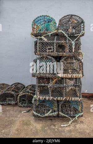 16 June 2022 Scarborough, North Yorkshire, UK - Lobster pots stacked on the quayside against a grey wall. Stock Photo