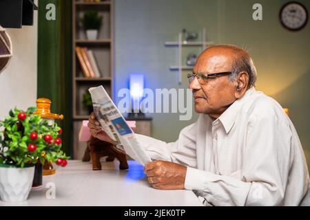 Old man with eyeglasses reading newspaper at home - concepts of daily routine, knowledge and relaxation Stock Photo