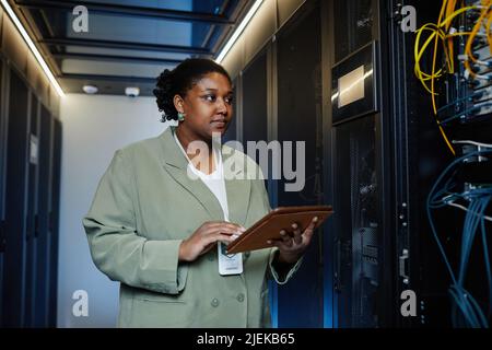 Waist up portrait of female IT technician using laptop in server room and managing company network, copy space Stock Photo