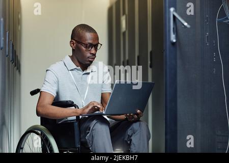Portrait of African American man with disability using laptop in server room while working as IT technician Stock Photo