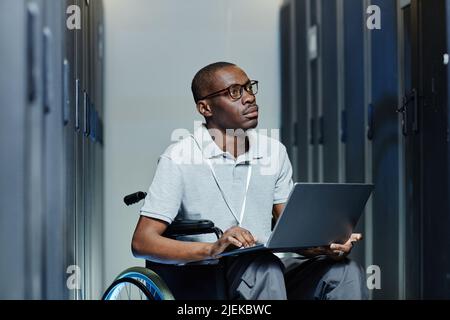 Minimal portrait of young black man with disability using laptop in server room while working as IT technician Stock Photo