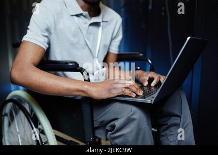 Cropped shot of black man with disability using laptop in server room while working as IT technician Stock Photo