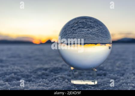 Crystal ball macro closeup of view in round glass globe on stand with reflection of Bonneville salt flats and mountains at colorful sunset in Utah des Stock Photo