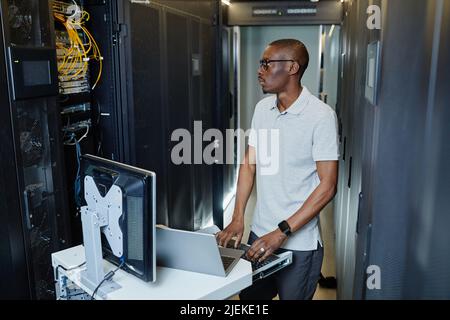 Side view portrait of black man connecting laptop to server cabinet and setting up internet network Stock Photo