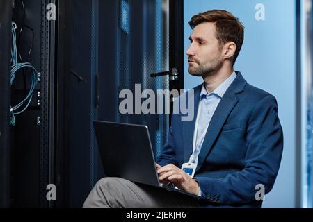 Side view portrait of IT system administrator using laptop in server room, copy space Stock Photo