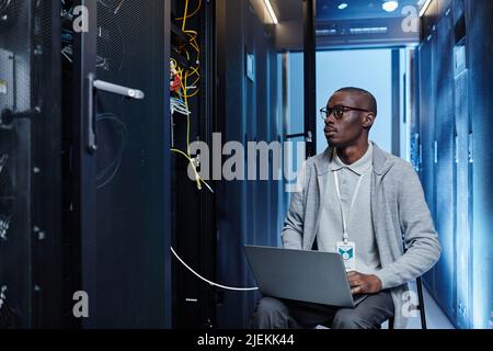 Portrait of black IT engineer setting up server network and using laptop in data center, copy space Stock Photo