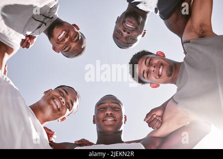 Portrait of sporty men from below joining in huddle for support and unity. Group of cheerful friends and motivated athletes collaborating together in Stock Photo