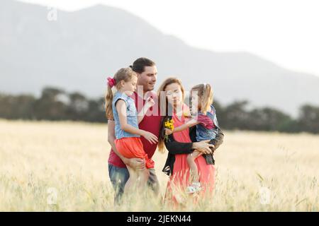Happy family father of mother and two daughters sisters on nature at sunset.Carefree parents having fun with their kids on a field. Stock Photo