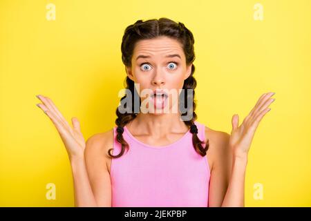 Photo of sweet impressed young woman pigtails wear tank top rising arms big eyes isolated yellow color background Stock Photo