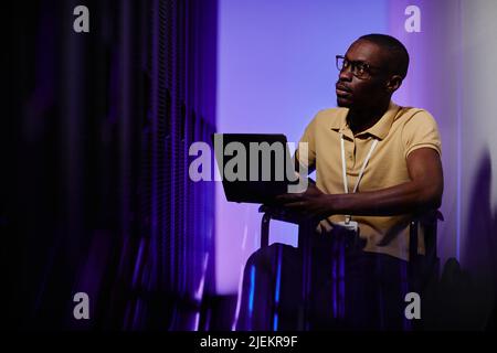 Portrait of black adult man with disability using wheelchair in server room lit by neon light, copy space Stock Photo