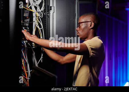 Side view portrait of adult African American man repairing server and setting up data network Stock Photo