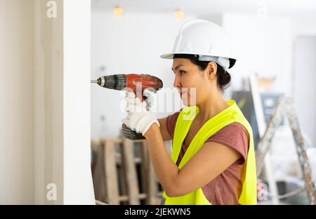 Woman builder using drill to bore hole in wall Stock Photo