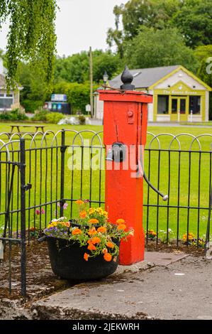 Traditional cow-tail water pump painted red on a village green. Stock Photo