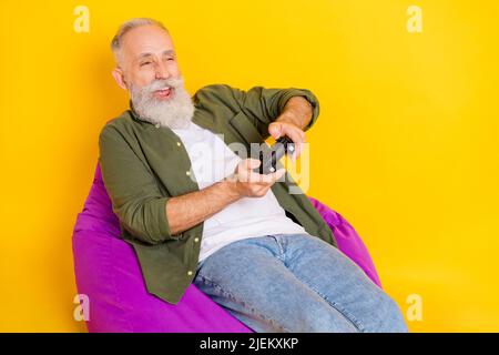 Photo of positive gamer old man hold gamepad play video game wear green shirt isolated yellow color background Stock Photo
