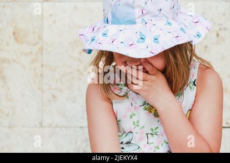 Sad European baby girl in colorful Panama hat, close-up face portrait Stock Photo