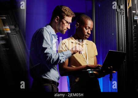 Waist up portrait of two network engineers using computer in dark server room lit by neon light, copy space Stock Photo