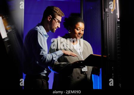 Waist up portrait of two system administrators using computer in dark server room lit by neon light, copy space Stock Photo