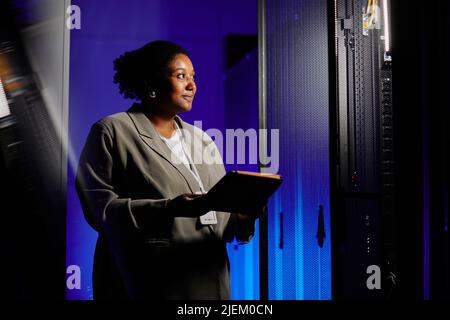 Waist up portrait of female system admin using tablet in server room lit by neon light, copy space Stock Photo