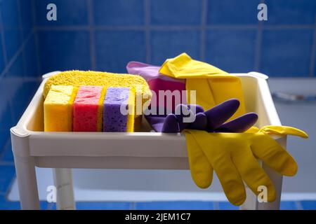 Rubber gloves and sponges on white shelf inside bathroom. Closeup. Set of colorful accessory for house cleaning. Clean house. Front view. Stock Photo