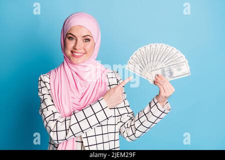 Portrait of pretty cheerful rich muslimah girl holding in hands demonstrating finance isolated over bright blue color background Stock Photo