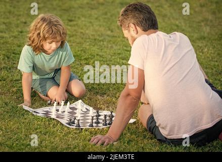 happy family of father man and son boy playing chess on green grass in park outdoor, opponent Stock Photo
