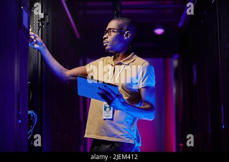 Side view of male system administrator setting up server network in data center lit by neon light Stock Photo