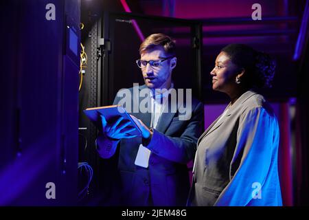Waist up portrait of two network engineers working in data center and setting up servers Stock Photo