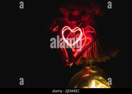 Red glass light bulb shaped like a heart glowing in the dark Stock Photo