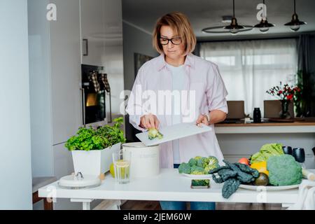 Compost the kitchen waste, recycling. Household woman scraping, throwing vegetables cutting leftovers into the garbage, compost bin while cooking on h Stock Photo