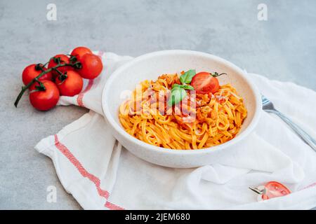 A plate of just cooked homemade fettuccine pasta with creamy tomato sauce, seafood and parmesan cheese, decorated with basil leaves on the grey stone Stock Photo