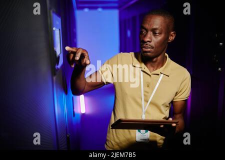 Waist up portrait of male system administrator setting up server network in data center lit by neon light Stock Photo