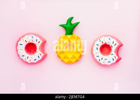 Top view inflatable toy rings on pink Background. Drinks Holders for Swimming Pool Party in Shape of Donuts and pineapple. Flat lay, selective focus, Stock Photo