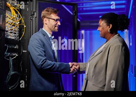 Side view portrait of two business partners shaking hands while standing in server room interior Stock Photo