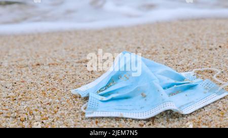 Coronavirus COVID-19 is contributing to pollution. Used face mask polluting tropical beaches. Polluted ocean coast with garbage. Environmental and Stock Photo