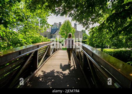 A lady wals over a bridge over the River Rye in the exterior of Nunnington Hall, a National Trust stately home in Yorkshire Stock Photo
