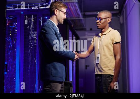 Waist up portrait of businessman shaking hands while employee in data center interior Stock Photo