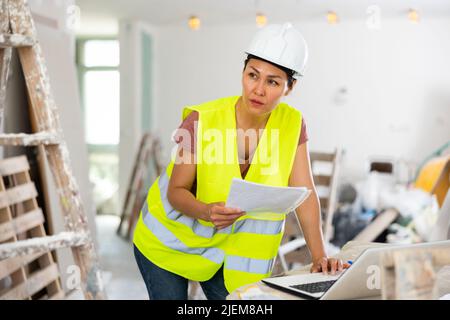 Woman builder checking project documentation and using laptop Stock Photo