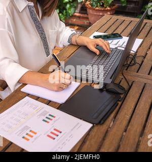 Woman teleworking in the garden of her house and writing down notes in a notebook. Stock Photo