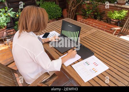 Woman teleworking in her home garden with documents and laptop Stock Photo