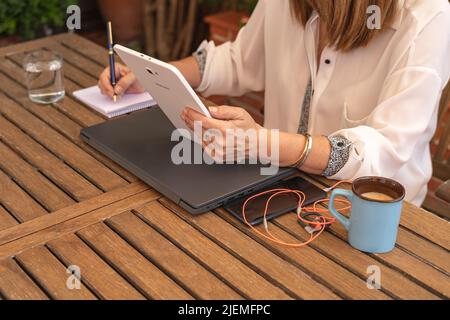 Woman teleworking and taking notes in a notebook from the garden of her house. Stock Photo