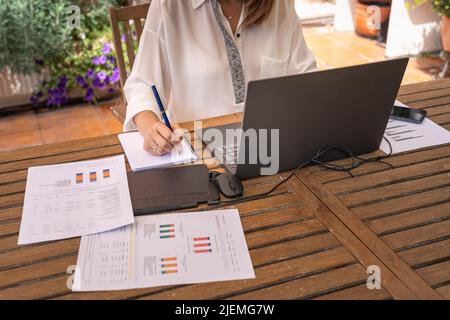 White woman teleworking in the garden with laptop and notebook. Stock Photo
