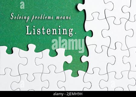 Motivational quote on white jigsaw puzzle with some missing pieces on purple background - Solving problems means listening. Stock Photo