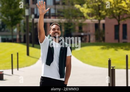 Happy african american guy waving hand and greeting friends outdoors, raising hand and smiling Stock Photo