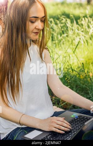 On the banner, a young girl works with a laptop in the fresh air in the park, sitting on the lawn. The concept of remote work. Work as a freelancer. T Stock Photo
