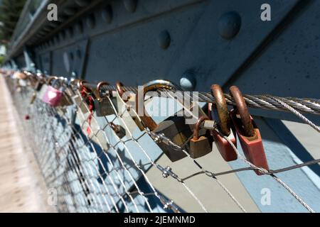 Close up of steel bridge railing with stretched wire mesh fence and closed locked shackle padlocks attached to it as concept for connection love and r Stock Photo