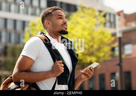 Handsome african american college guy using smartphone outdoors, walking in urban area after classes Stock Photo
