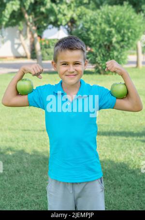 Funny boy with green apples shows biceps. Vertical shot. Stock Photo