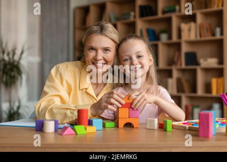 Happy little girl and female supportive child development specialist smiling at camera, playing with colorful bricks Stock Photo
